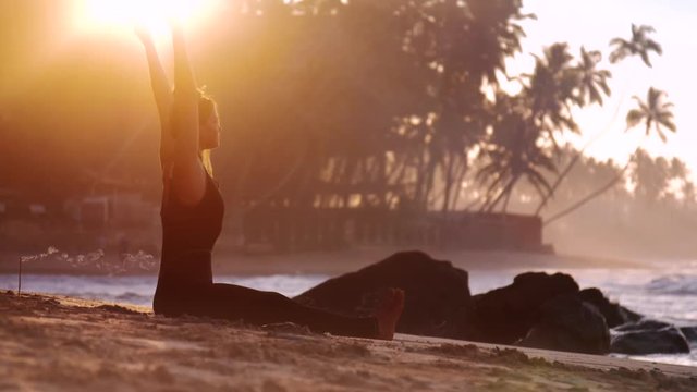 tremendous lady practices yoga on sandy beach near stones and ocean waves in tropical morning slow motion. Concept fitness sport yoga wellness healthy life