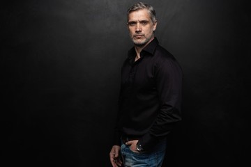 Middle-aged good looking man posing in front of a black background with copy space.