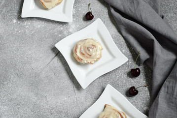Cinnamon bun in a square plate on a gray background, decorated with a linen towel and cherry. Horizontal image. Copy space. Flat lay.