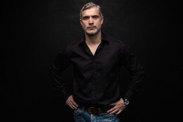 Fototapeta premium Middle-aged good looking man posing in front of a black background with copy space.