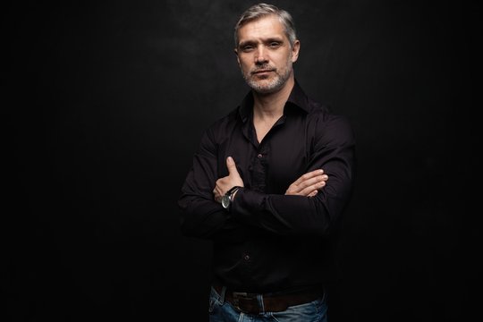 Middle-aged good looking man posing in front of a black background with copy space.