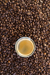 Espresso shot on a table filled with roasted coffee beans. High resolution