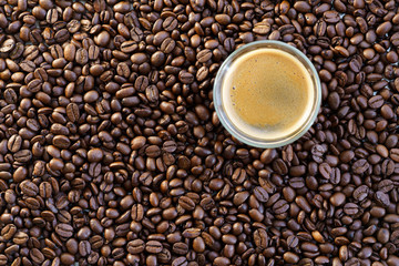 Espresso shot on a table filled with roasted coffee beans. High resolution