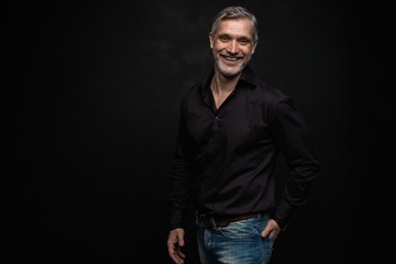 Fototapeta premium Middle-aged good looking man posing in front of a black background with copy space.