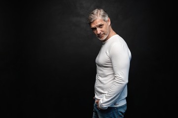 Middle-aged good looking man in white t-shirt posing in front of a black background with copy space.