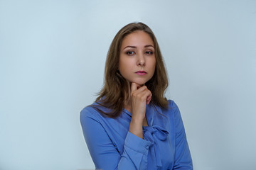 Girl with brown hair in blue blouse thinks in studio on gray background. Business portrait photography of science person 