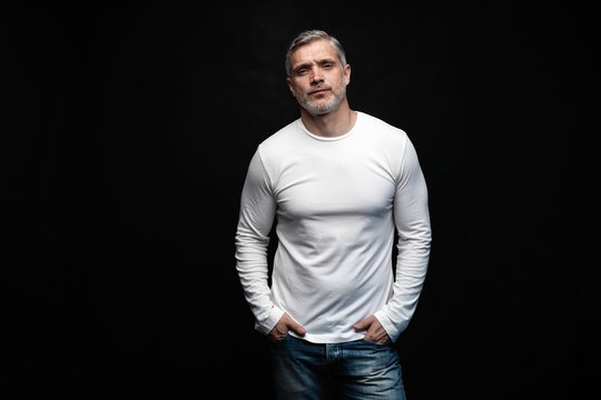Middle-aged good looking man in white t-shirt posing in front of a black background with copy space.