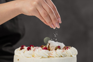 The condater sprinkles the cake with grated almonds and coconut. Close-up of a hand and pouring crumbs.