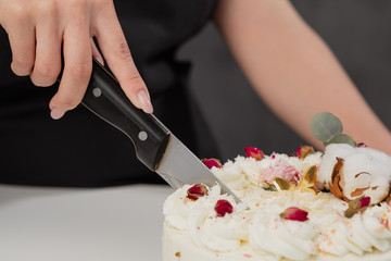 A condater cuts a beautiful fresh decorated white cake with a large knife.