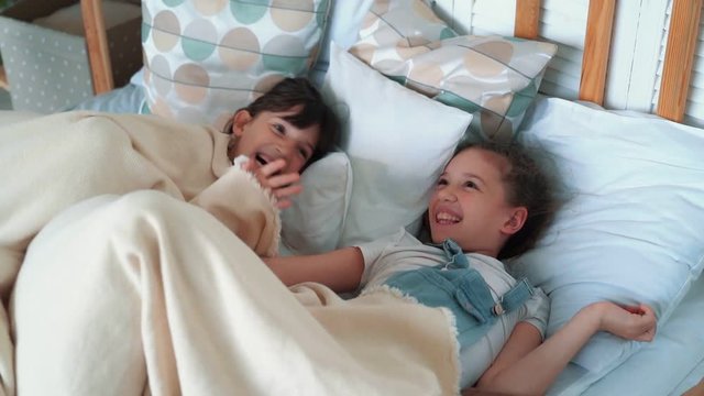 Two little cute girls lies in bed, smile and laugh, slow motion