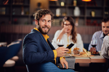 Young smiling Caucasian man dressed smart casual using smart phone and looking over shoulder while...
