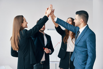 Smiling young business people giving high five to each other in office