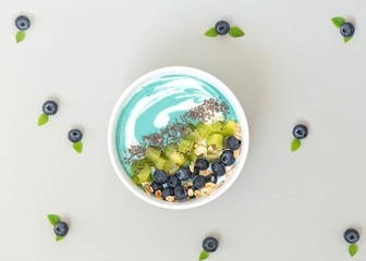 Top view of blue spirulina smoothie bowl with blueberries, kiwi, Chia seeds and granola on grey table. Healthy breakfast. Vegan food. 