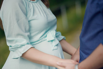 Cropped shot of handsome Caucasian couple holding hands with focus on the pregnant woman's beautiful round tummy, concept for happy family expecting a baby, couples pregnancy or proud of baby bump