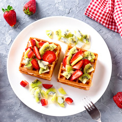 Belgian waffles with fruits strawberries and kiwi on white plate closeup. Tasty healthy breakfast