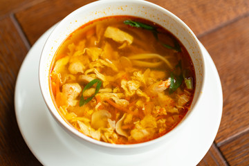 Asian noodle soup with chicken, vegetables and egg in a bowl on a wooden table.