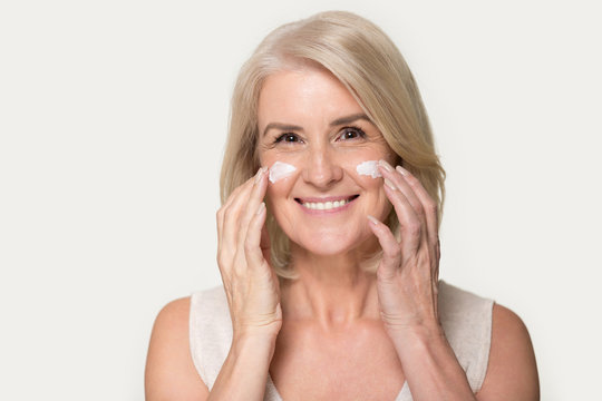 Happy mature woman looking at camera applying anti-aging cream