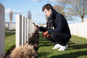 Man looking up information on mobile phone about soldier grave at military cemetary
