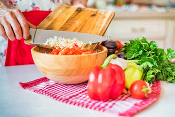 Female hand put chopped garlic in wooden bowl with salad in kitchen. Cooking vegetables