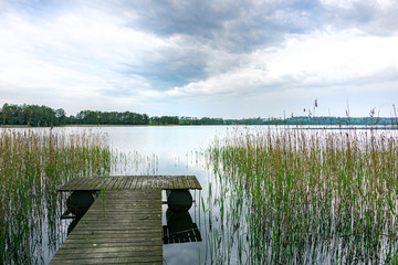 Obraz premium Beautiful view of the lake, wooden pier and water grass. Spring, Mazury, Poland.