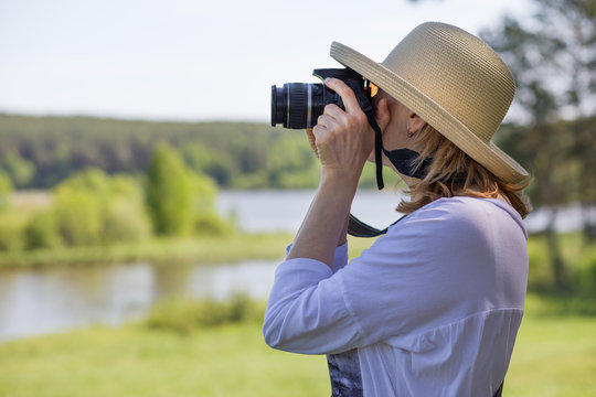 An elderly woman with a camera taking pictures of nature and enjoying life.