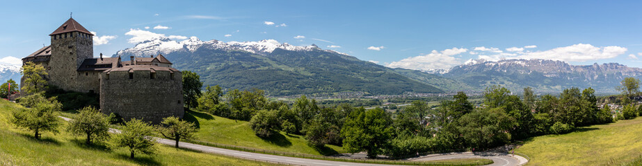 Panorama of an alpine landscape with high mountains and castle, green meadows and trees in spring with snow in the Liechtensteiner and Swiss Alps