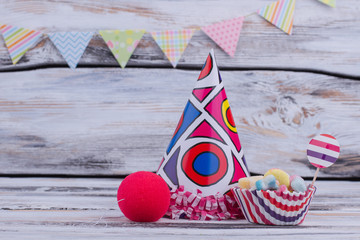 Background with kids Birthday party items. Party hat, sweeets and clown sponge nose on wooden background. Childrens Birthday supplies.