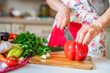 Female hand with knife cuts bell pepper in kitchen. Cooking vegetables