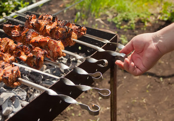 On the barbecue, a lot of meat is roasted on skewers, the chef turns over his shish kebabs. A man's hand turns, fries tasty meat of pork on skewers.