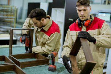 Two young workers assembling furniture in the factory