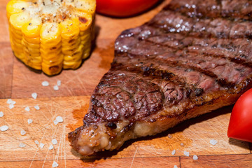 Close up freshly grilled steak on wood with tomatoes and corn