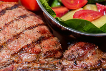 Close up freshly grilled bone steak on wood and fresh salad in bowl
