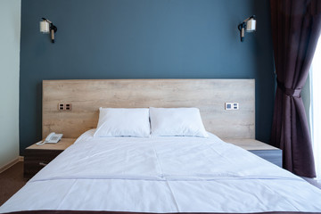 Double wooden bed, with white pillows, bedside tables on the sides, against the blue wall with lamps.