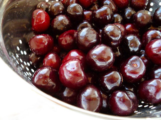 Ripe Red Sweet Cherries in metal colander with water drops isolated on white. Close-up of fresh red sweet cherries in metal colander on white surface. Fresh summer background. 
