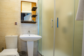 Beige bathroom with glazed shower, mirror over the sink, towel and toilet.