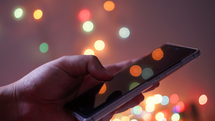 woman holding and using her mobile phone at night and bokeh light background