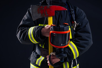Fototapeta premium portrait strong fireman in fireproof uniform holding an ax chainsaw in his hands black background studio
