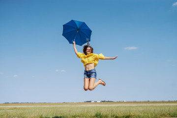 Cheerful Caucasian teenage girl in yellow blouse, denim shorts and with eyeglasses jumping outdoor...