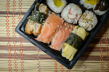 Set of various rolls in black plastic box. Rolles collection with crab sticks, salmon, sockeye salmon, coho salmon, masago caviar, wakame, shiitake mushrooms, eel, radish, nori seaweed.