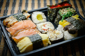 Set of various rolls in black plastic box. Rolles collection with crab sticks, salmon, sockeye salmon, coho salmon, masago caviar, wakame, shiitake mushrooms, eel, radish, nori seaweed.