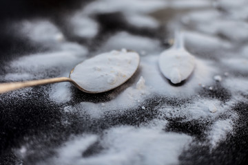 Raw powdered baking soda in a antique spoon on wooden surface along with some more in a plastic...