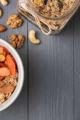 Granola cereal flakes with dried fruit, nuts in green bowl on gray wooden table. Top view with copyspace.