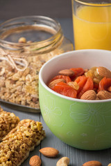 Granola cereal flakes with dried fruit, nuts in green bowl on gray wooden table.