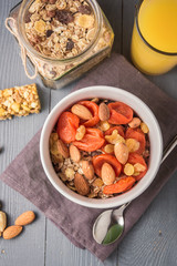 Granola cereal flakes with dried fruit, nuts in green bowl on gray wooden table. Top view.