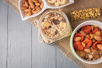 Granola cereal flakes with dried fruit, nuts in green bowl on gray wooden table. Top view with copyspace.