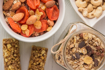 Granola cereal flakes with dried fruit, nuts in green bowl on white wooden table. Top view.