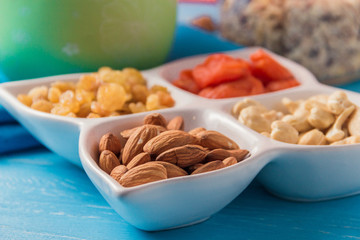 Granola cereal flakes with dried fruit, nuts in plate on blue wooden table.