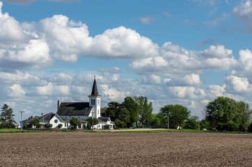 Beautiful, white church in a country, rural setting surrounded by farm fields and trees. Bright...