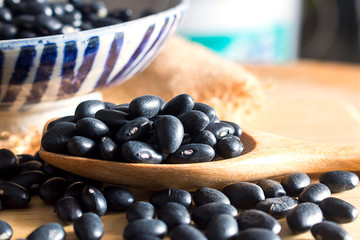 Raw black beans in wooden spoon on table.