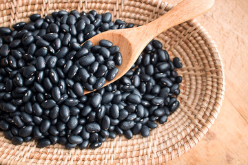 Raw black beans in basket and spoon on wood table.